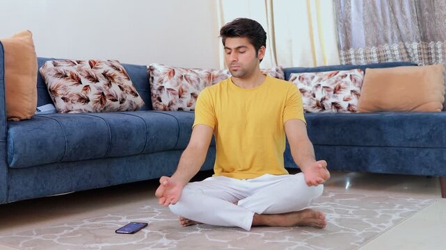 Adorable young guy interrupted by a phone call while meditating in the living room. Handsome Indian man answering an important phone call while doing breathing exercises - lifestyle concept