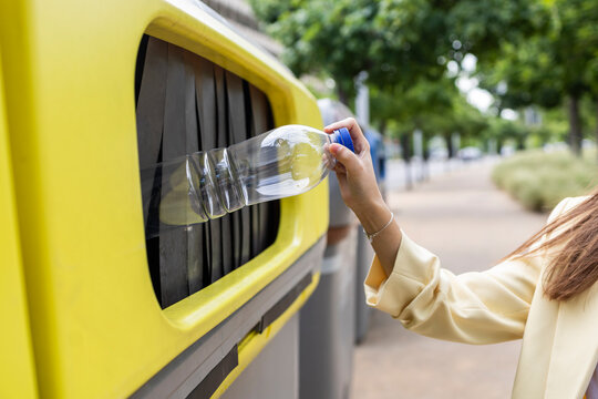 Young woman recycling plastic bottle in colorful street bin