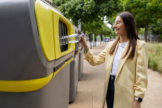 Young woman recycling plastic bottle at colorful city bins