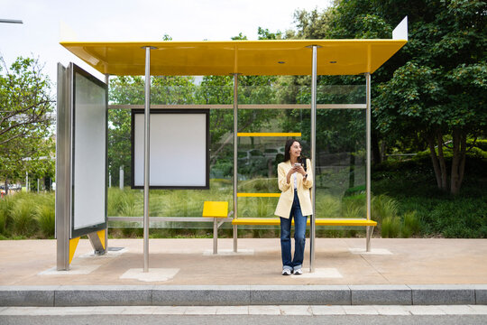 Young woman waiting at colorful modern bus stop in park