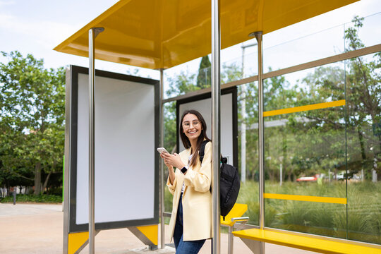Young colorful woman using smartphone at modern bus stop