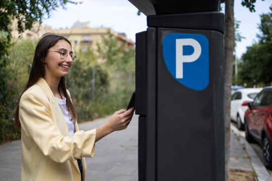 Young woman using parking meter on city street