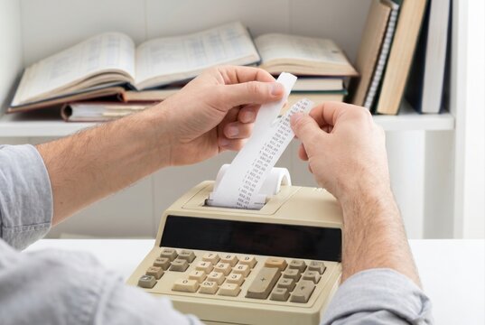 Male hands holding paper tape from an adding machine checking financial data and accounting numbers
