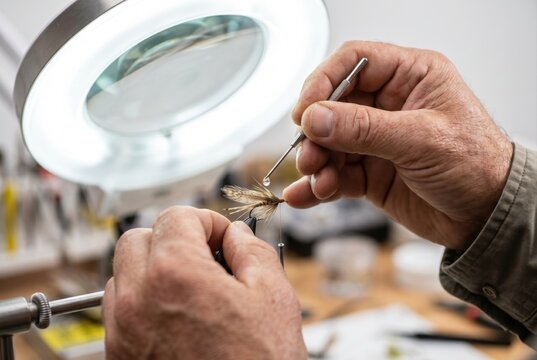 Close up of hands using a fine needle under a magnifying lamp to tie a fishing fly lure