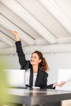 Smiling businesswoman with raised hand in modern office
