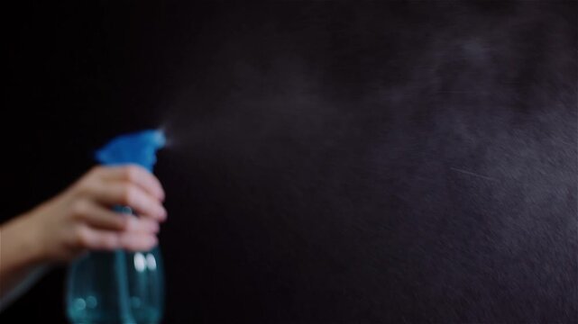 Hand spraying cleaner onto a dark surface in close-up