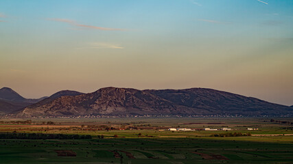 Fototapeta premium Wide landscape view of an agricultural valley plain against a massive karst mountain range at sunset.