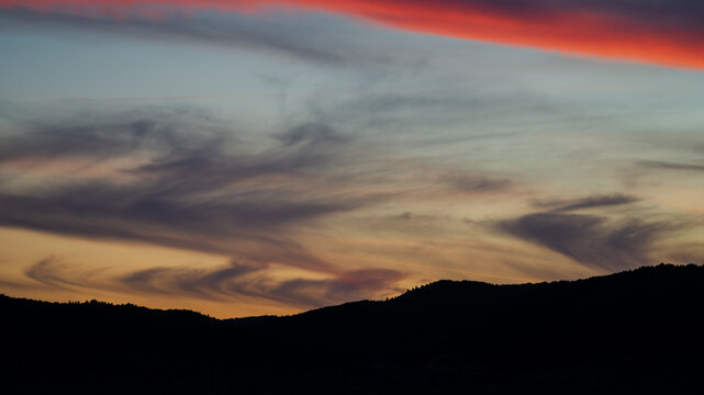Beautiful sunset sky gradient with wispy clouds over dark mountain silhouettes and a fiery red cloud streak.