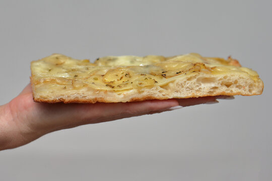 Woman's hand holding a fluffy slice of thick Roman-style potato pan pizza on a neutral background