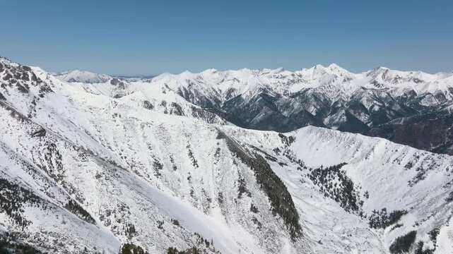 Aerial footage of snow covered Peak Galina and rugged mountain ridge near Arshan village, Republic of Buryatia, Russia, with clear blue sky and alpine panorama
