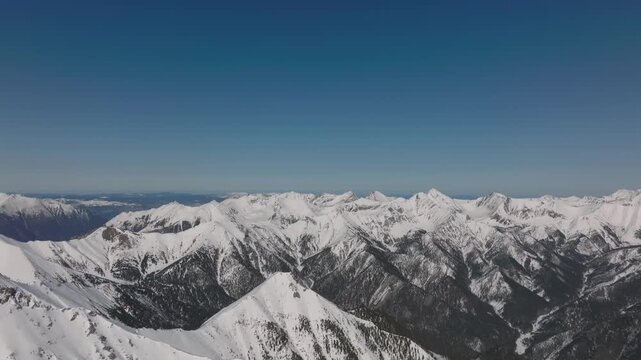 Wide aerial footage of Galina Peak and surrounding snow-covered ridges near Arshan, Republic of Buryatia, Russia, with clear blue sky and dramatic alpine landscape