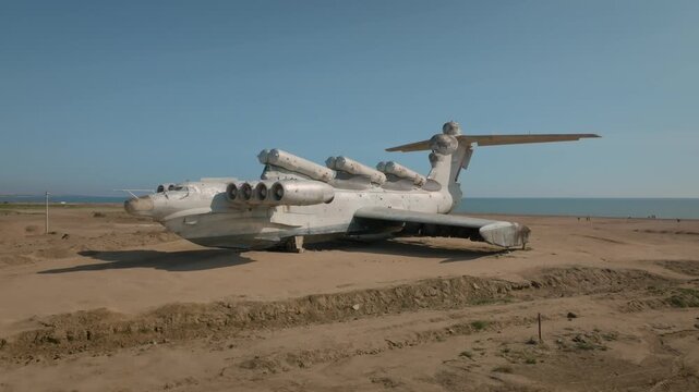 Wide shot of the abandoned Soviet Lun-class ekranoplan on a sandy shore by the Caspian Sea in Derbent, Republic of Dagestan, Russia, clear blue sky