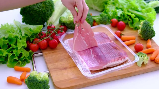 Taking thin jamon slices from package beside farm vegetables on rustic kitchen board