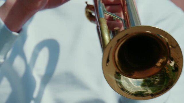 Close up of a brass trumpet bell reflecting the surrounding environment, with soft natural light highlighting metallic textures