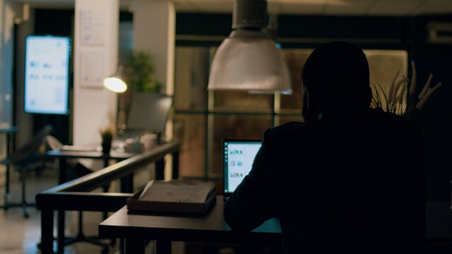Employee left alone in the dark overnight in office, solving project tasks before next day deadline. Accountant working by himself in workspace, trying to keep up with paperwork