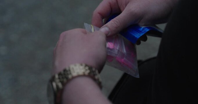 Close-up of unidentified pink tablets stored in a small plastic bag and held in hands. Concept of illicit substances, drug abuse, narcotics, addiction, law enforcement, and public health concerns.