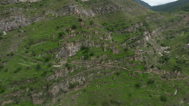 Drone footage of the abandoned stone aul of Kahib on a steep green mountainside, with terraced ruins and paths in the Caucasus, Dagestan, Russia