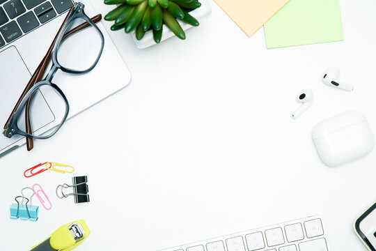 Top view workspace mockup with laptop, wireless earbuds, succulent, and colorful stationery on a white desk with copy space