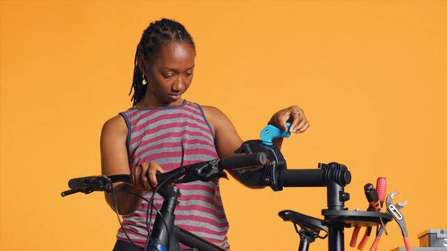 African american woman setting up bike repair stand, using it to adjust derailleur, fixing broken wheels, studio background. Professional placing bicycle on workstand to do checkup on it, camera A