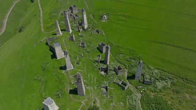 Drone footage of the medieval Erzi tower complex with stone watchtowers and ruins on a lush alpine hillside in Republic of Ingushetia, Russia