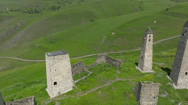 Drone footage of the medieval Erzi tower complex with ancient stone watchtowers and ruins on green hills in Ingushetia, Russia