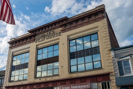 Suffern, NY - US - May 31, 2026 An urban brick building features Hines Playhouse, Suffern Supermarket, a law office, and Licata Insurance. The sky is bright blue with light clouds, framing the facade.