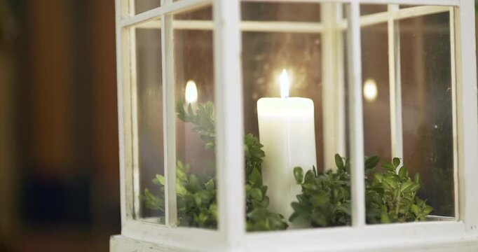 Warm candle glowing in a glass lantern with greenery