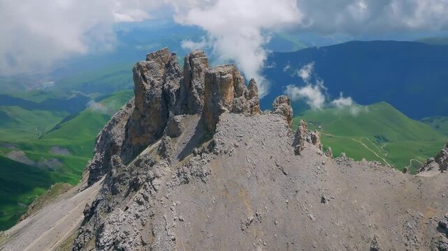 Drone footage of jagged rock spires and scree ridge on Mount Naudzhidza above green alpine valleys and drifting clouds in Kabardino-Balkaria, Russia