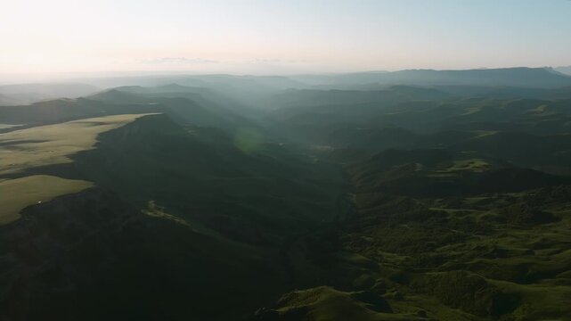 Drone footage of layered mountain ridges and deep valleys in soft morning haze at Bermamyt Plateau, Karachay-Cherkessia, Russia, wide scenic landscape