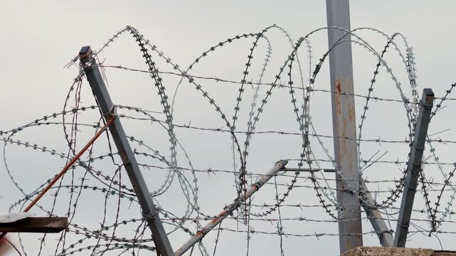 A sharp close up of barbed wire stretched across a fence, with a blurred building in the background