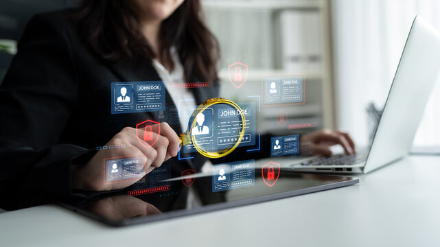 Business Professional Analyzing Digital Data with a Magnifying Glass on a Tablet Displaying User Profiles and Security Icons in an Office Setting. Entropy.