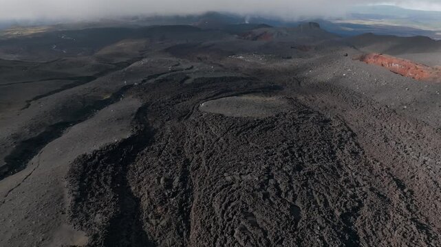 Drone footage of rugged basalt lava flows, cinder cones and volcanic craters at Tolbachinsky Dol, Kamchatka Krai, Russia, under low clouds and haze