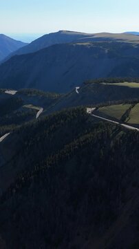 Vertical Screen: Beartooth Highway winds through forested Montana USA mountains with dramatic switchbacks cutting across steep ridges under clear blue skies in stunning aerial perspective.