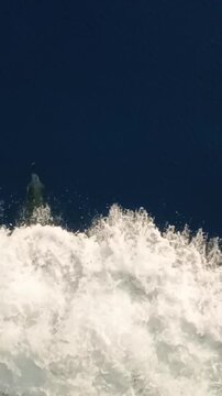 Vertical slow motion of playful dolphins jumping out of the ocean water near a moving boat.