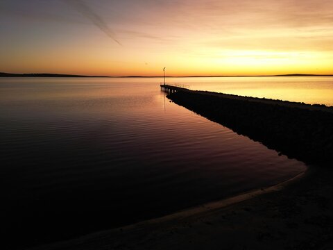 Aerial drone view of a stone and wooden jetty stretching into calm ocean waters at sunrise, Boston Bay, Spencer Gulf, South Australia