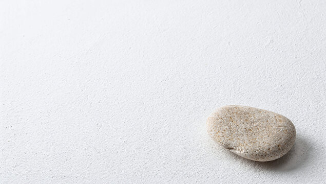 Single smooth sea pebble on white textured plaster surface