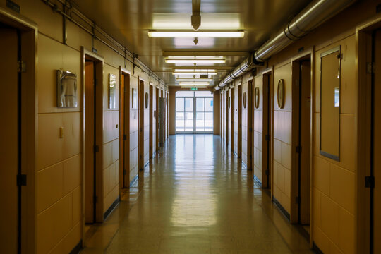 Long, empty hotel or dormitory corridor with many doors and fluorescent lighting hallway interior