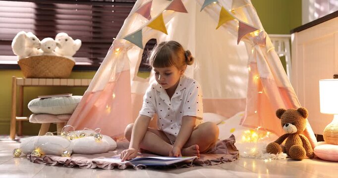 Little girl reading book in wigwam indoors