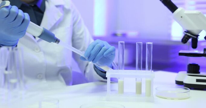 Laboratory testing. Scientist taking sample of milk at white table indoors, closeup. Camera moving left