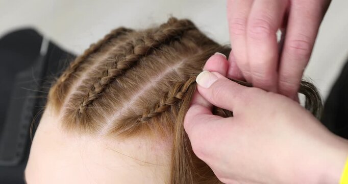 Hairstylist braiding teenage girl's hair indoors, closeup