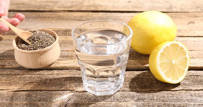 Woman pouring water into glass and adding chia seeds at wooden table, closeup