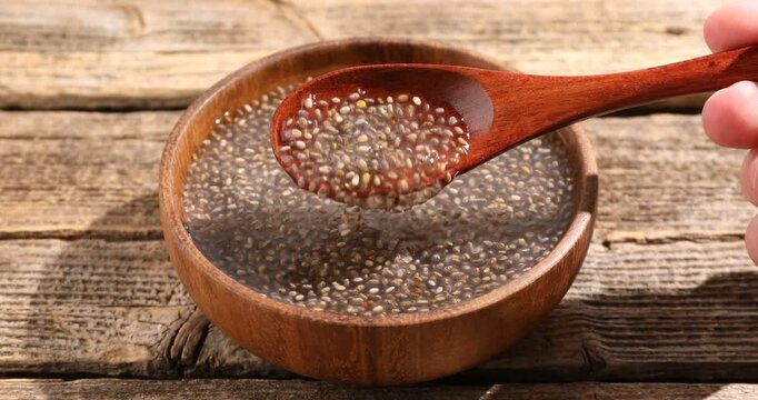 Woman stirring water with chia seeds at wooden table, closeup