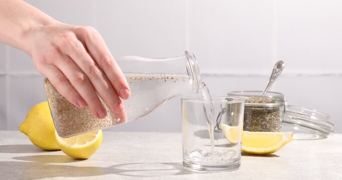 Woman pouring water with chia seeds into glass at light table, closeup