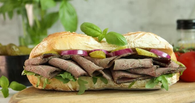 Woman putting delicious sandwich with pastrami (cured beef meat), pickles and onion on table, closeup
