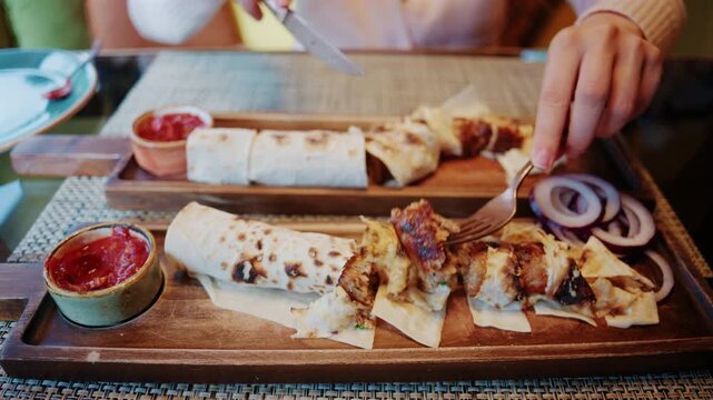 Close up of a freshly prepared wrap being sliced into portions on a wooden serving board, with sauces and side ingredients placed nearby
