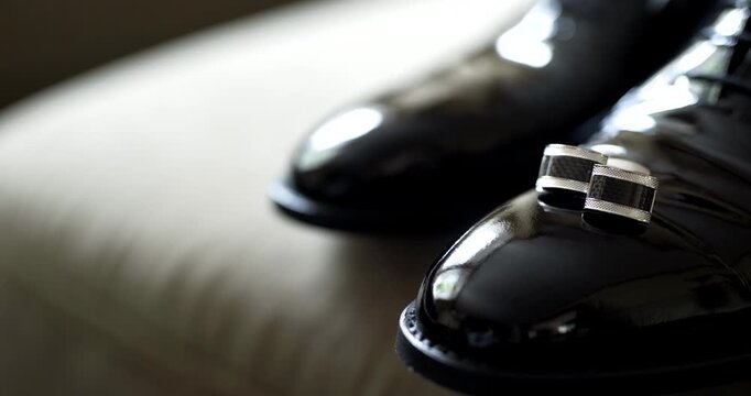 Polished black dress shoes and cufflinks on a light bed