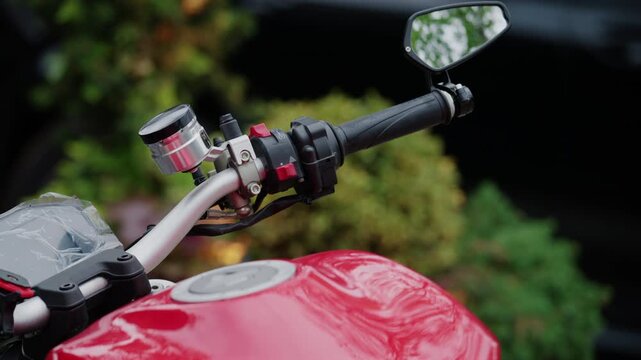 Close up detail of a motorcycle handlebar with visible control switches, mirror, and metallic components