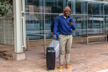 African American men on plaza by glass facade checking phone, pulling black and silver suitcases © wavebreak3