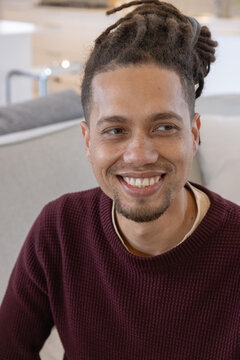 African American man sitting on light sofa smiling, looking right in lounge, wearing maroon sweater