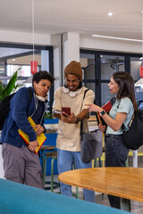 Diverse students leaning in, showing red phone in campus lounge, holding notebooks and backpacks © wavebreak3